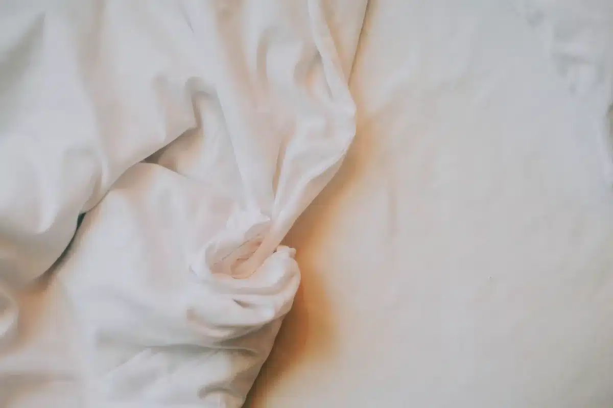 Drap plat en coton blanc sur un lit, montrant sa légèreté et sa maniabilité pour ajuster la couverture.