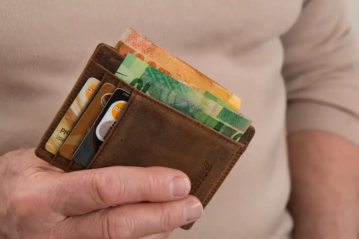 Portefeuille ouvert sur une table en journée avec un carton rigide derrière des billets